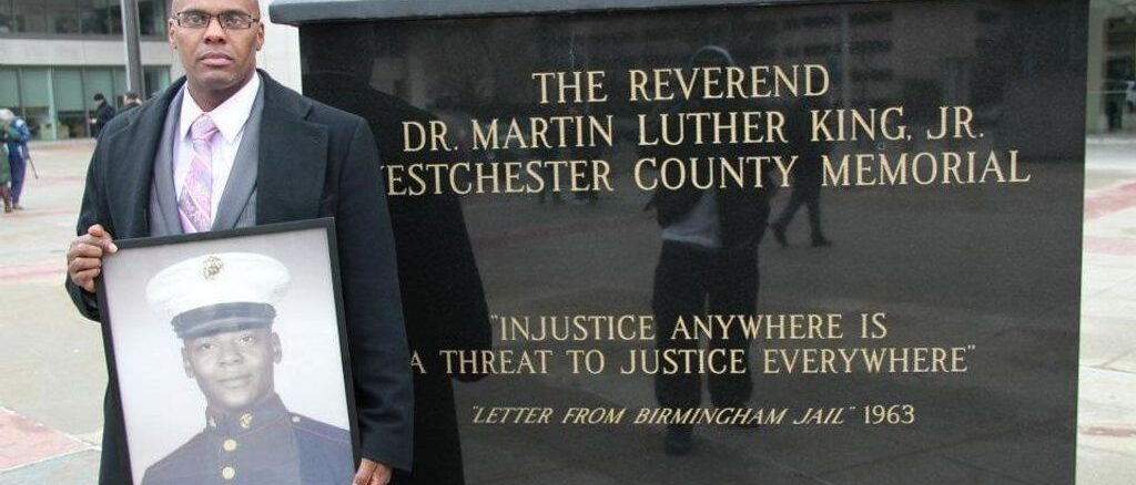Kenneth Chamberlain Jr. holds a photo of his father when he served as a U.S. Marine. He is standing by a stature of Dr. Martin Luther King Jr. in front of the Westchester County Courthouse in White Plains, New York. (Courtesy of Kenneth Chamberlain Jr.) 