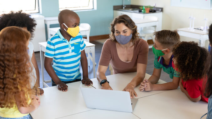 Female teacher wearing face mask using laptop to teach students