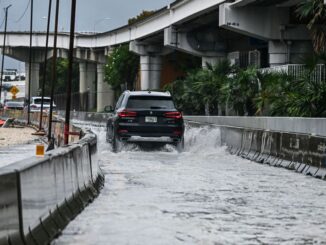 A car drives through the flooded street during heavy rain in Miami, Florida, on April 12, 2023. CHANDAN KHANNA/BENZINGA